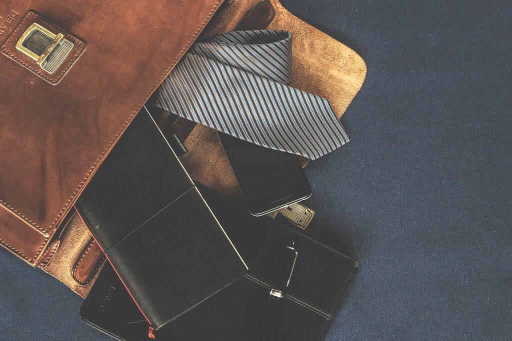 Flat lay of men's leather bag with accessories like a tie, notebook, and phone. Ideal for business themes.